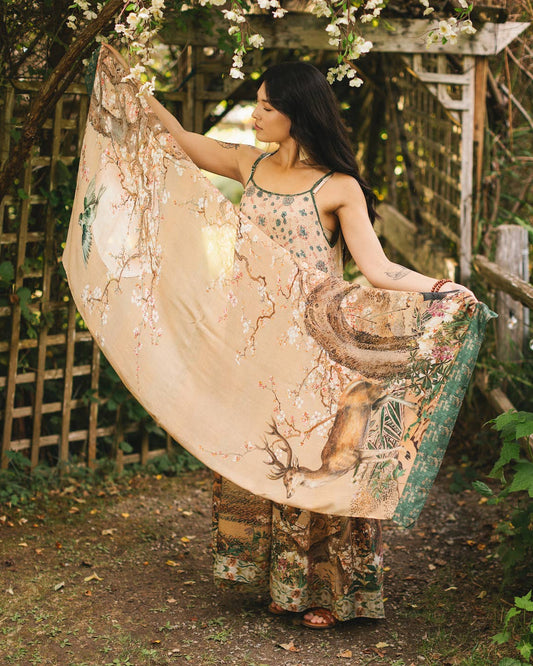 Woman in a floral dress holding a large, decorative fan in a garden setting.