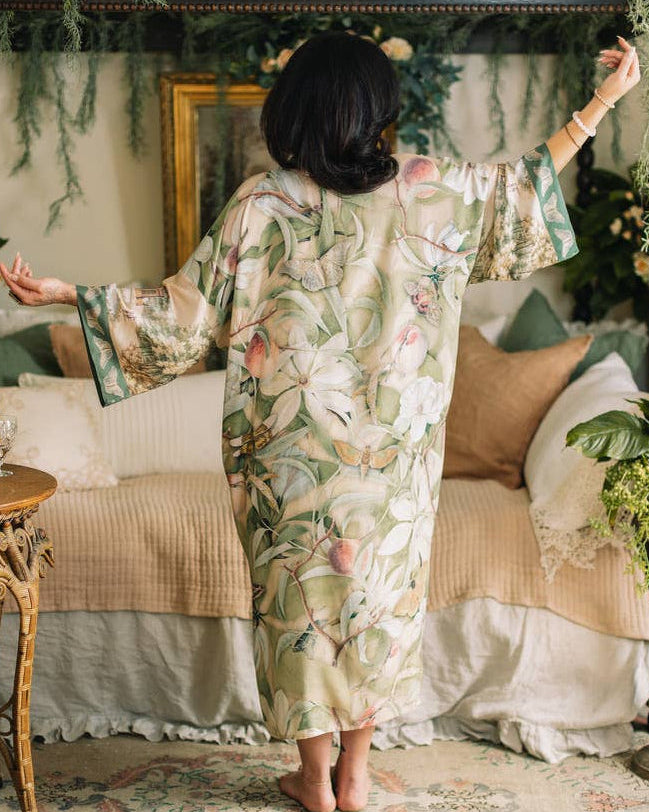 Woman in a floral kimono standing in a decorated room with plants and furniture.