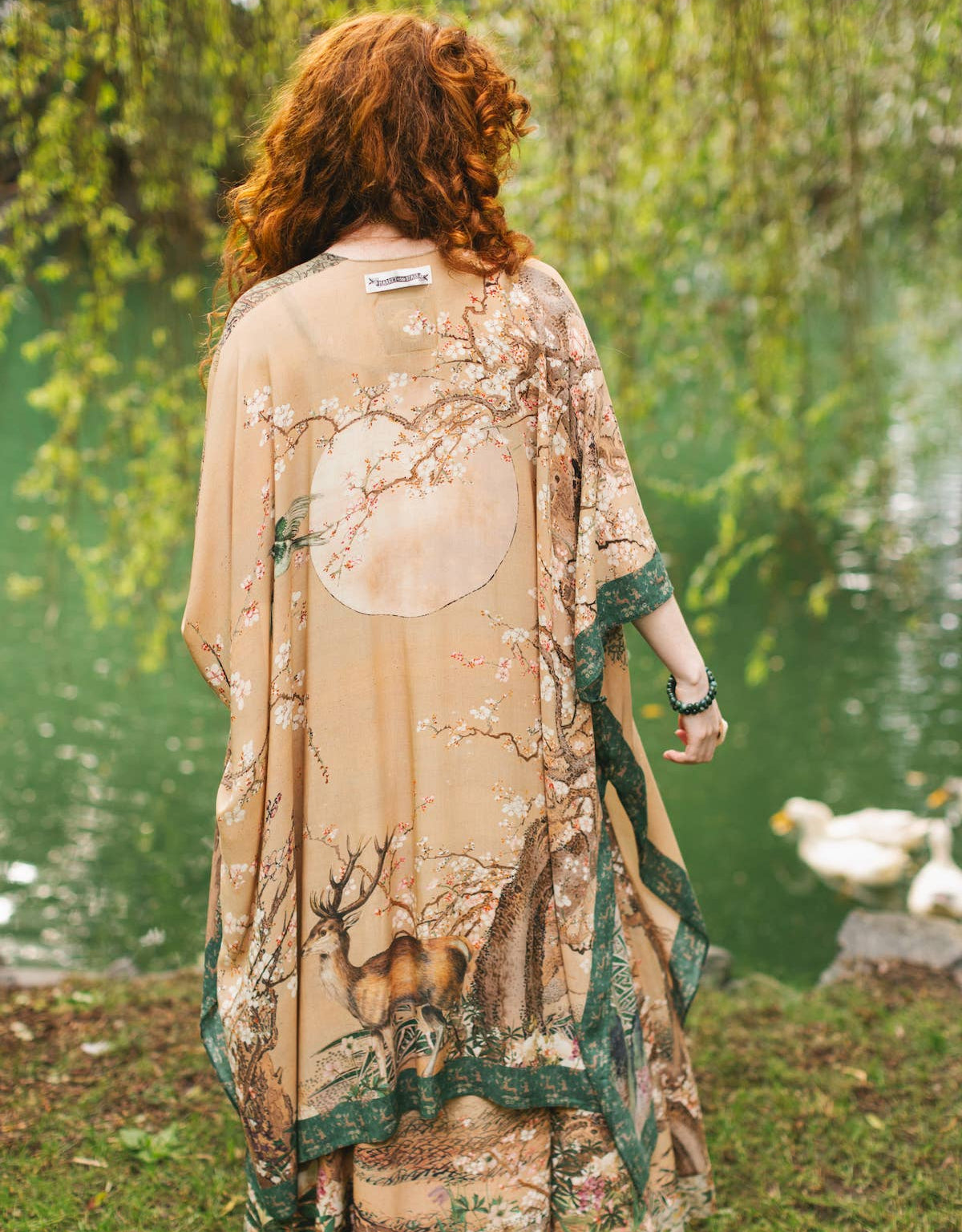 Person wearing a long, patterned kimono standing by a pond with ducks.